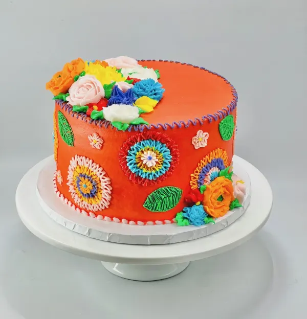 Round cake iced in bright orange buttercream with piped folk-art flowers and rosettes