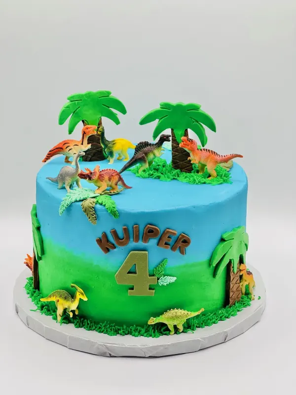 Dinosaur birthday cake with toy dinosaurs, fondant palm trees and KUIPER 4 on blue and green