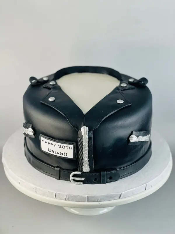 Cake shaped like a black leather biker jacket with a HAPPY 50TH BRIAN patch