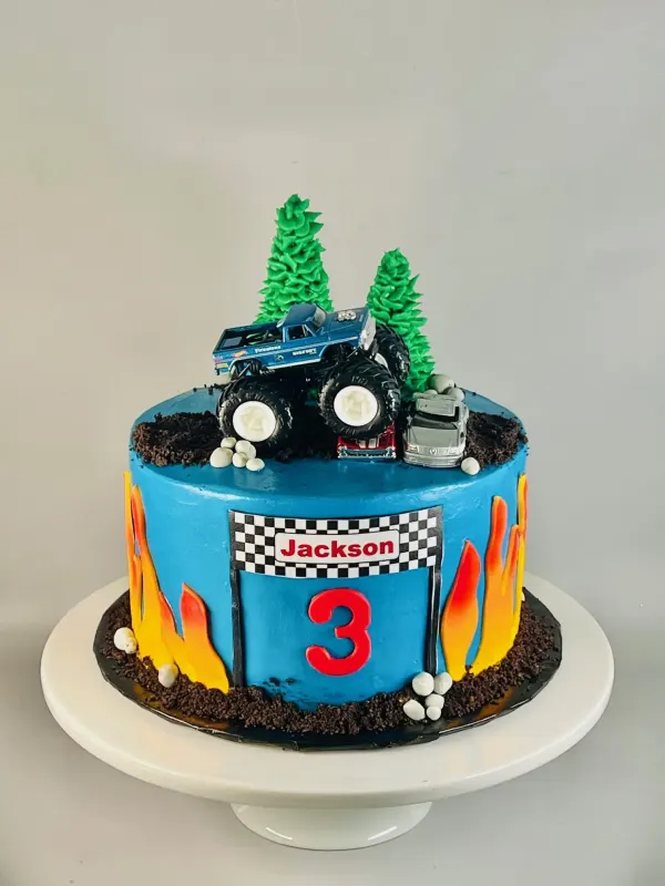 Monster truck cake in blue with fondant flames, buttercream pines and a Jackson 3 race sign