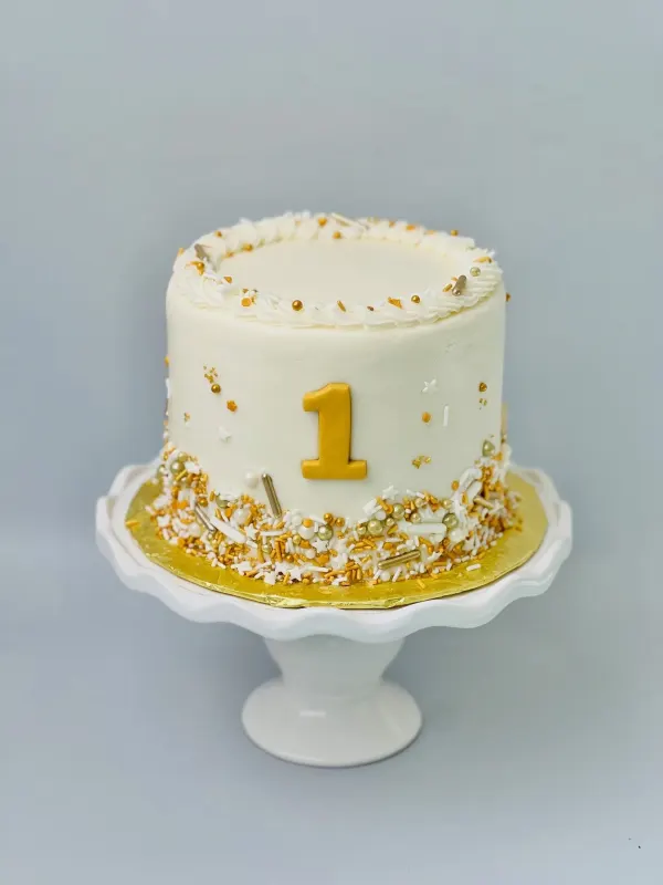 First birthday cake in white buttercream with a gold number 1 and gold and white sprinkles