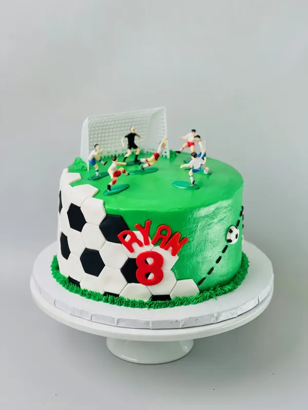Soccer cake with a green field, fondant ball panels, player figures and RYAN 8 in red