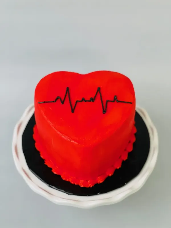 Red heart-shaped cake with a black heartbeat line piped across the top