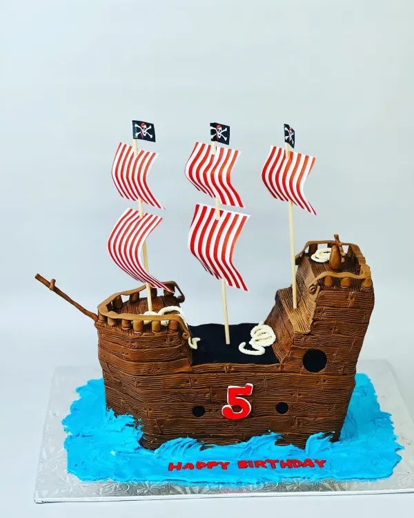 Pirate ship cake in wood-textured chocolate with striped sails, number 5 and Happy Birthday