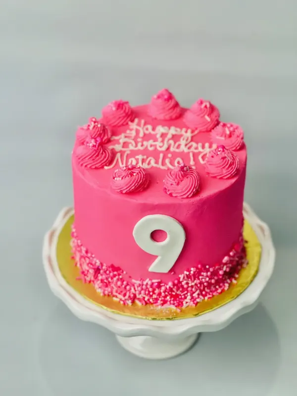 Hot pink cake with a white number 9, pink sprinkles and Happy Birthday Natalie piped on top
