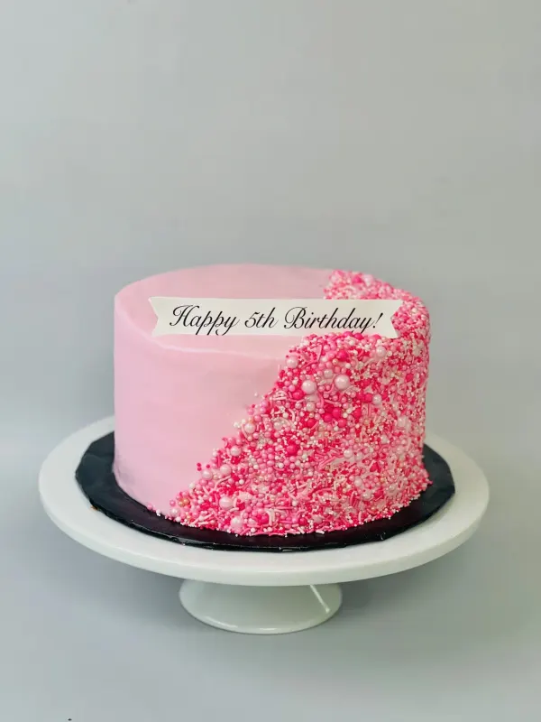 Pink birthday cake with a cascade of pink sprinkles and pearls and a Happy 5th Birthday banner