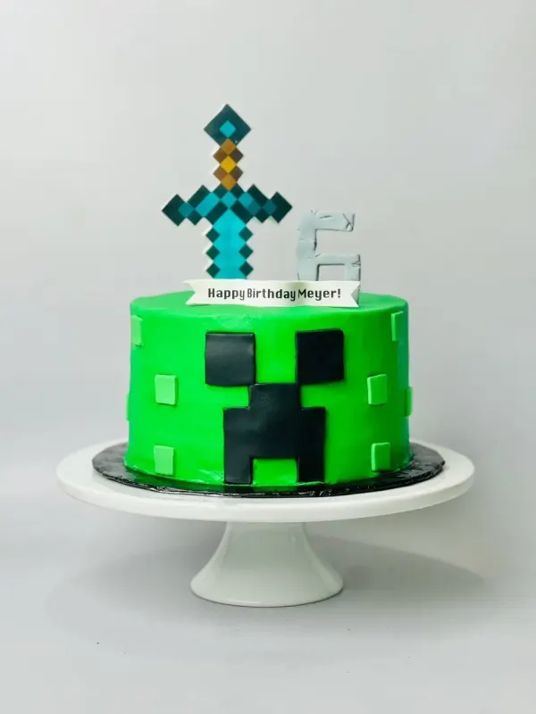 Minecraft creeper birthday cake in green with a pixel sword topper reading Happy Birthday Meyer