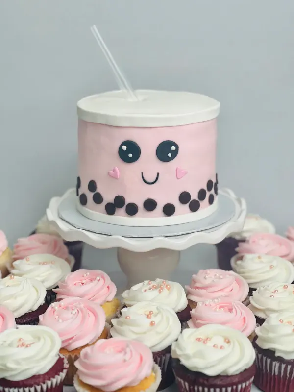 Boba tea cup birthday cake in pink with a smiling face, tapioca pearls and rosette cupcakes