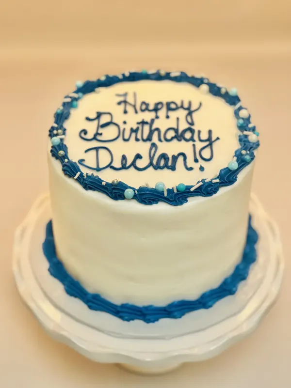 Round white buttercream cake with blue piped shell borders and Happy Birthday Declan in script