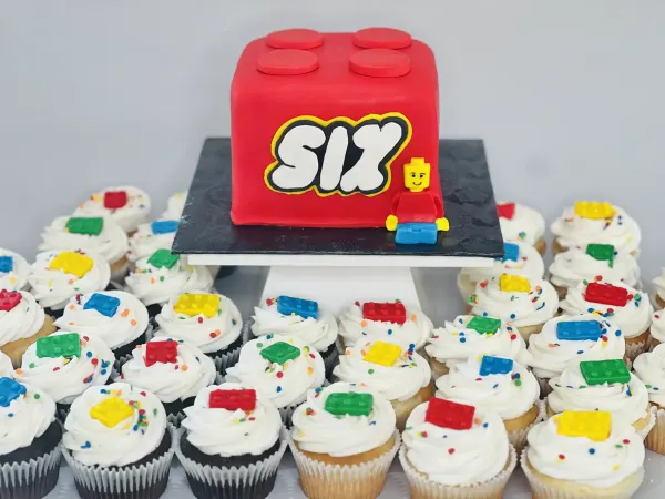 Red Lego brick birthday cake reading SIX with a minifigure and matching Lego brick cupcakes