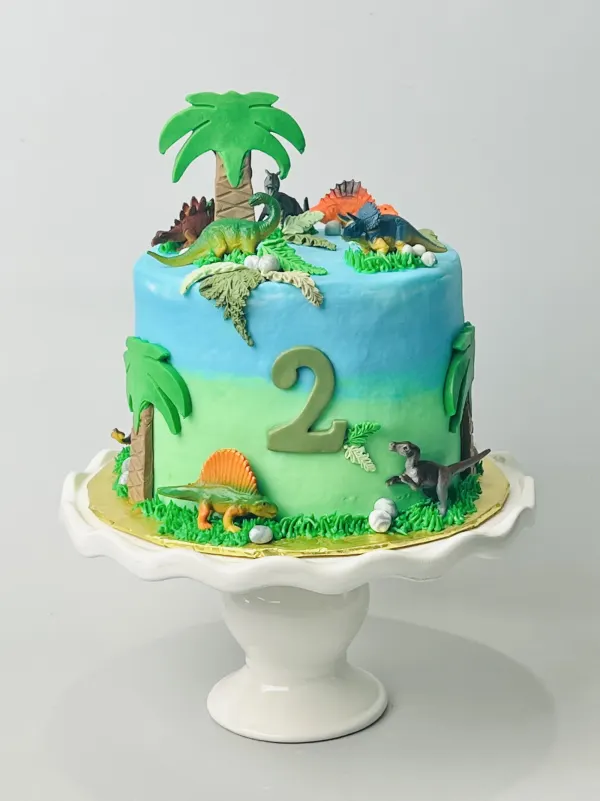 Dinosaur birthday cake with blue and green ombre buttercream, toy dinosaurs, palm trees and a number 2