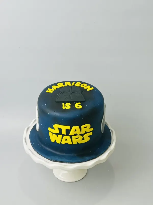 Navy Star Wars birthday cake with a Darth Vader helmet and yellow lettering reading Harrison is 6