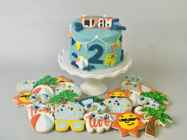 Teal pool party cake with sunglasses reading Liam, a number 2 and beach ball, with summer cookies