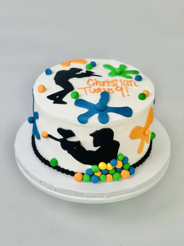 Round paintball birthday cake with black player silhouettes, paint splatters and Christian Turns 9