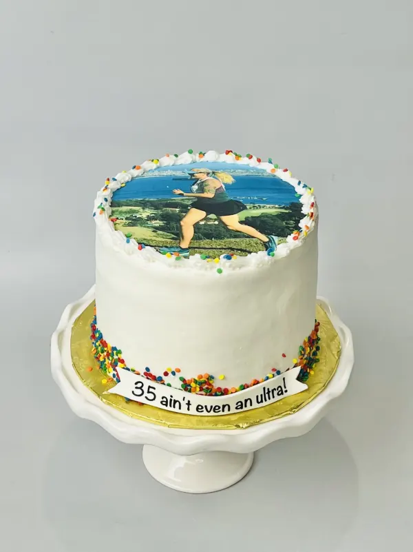 White birthday cake with an edible photo of a runner and a banner reading 35 ain't even an ultra