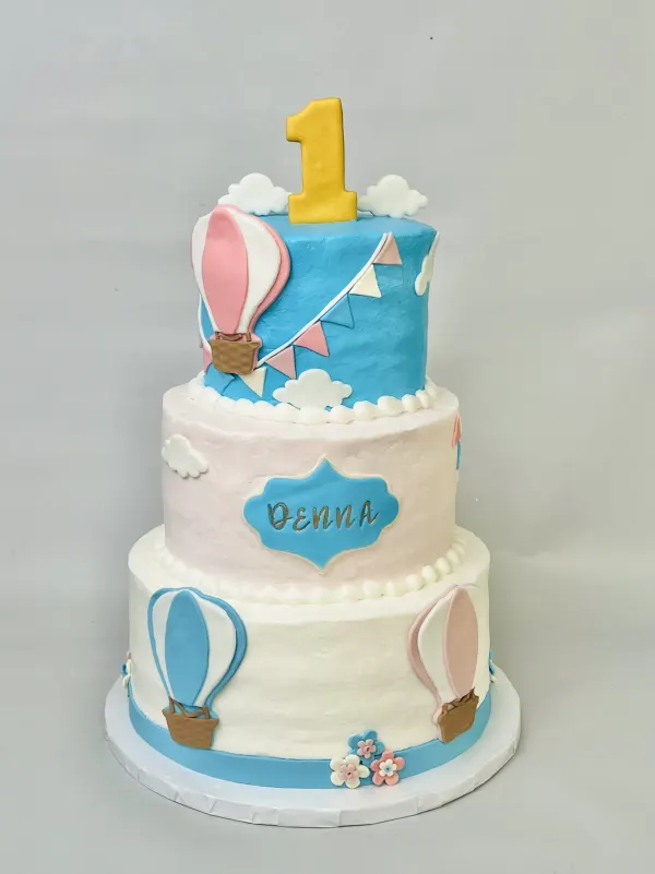 Three-tier hot air balloon first birthday cake with fondant balloons and a plaque reading Denna