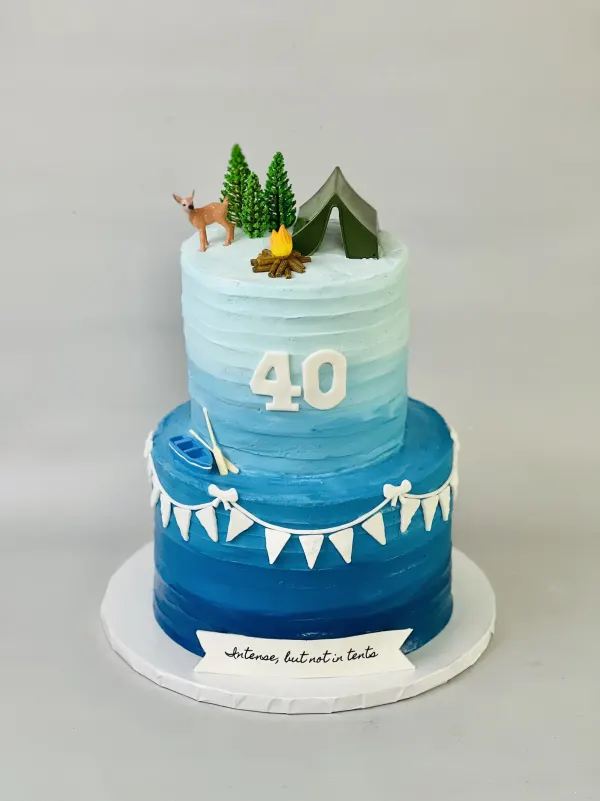 Two-tier blue ombre camping 40th cake with a tent, campfire and Intense but not in tents banner