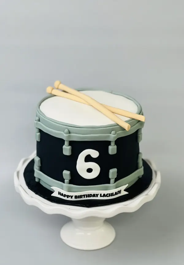 Snare drum cake in black and grey with fondant drumsticks, a white 6 and Happy Birthday Lachlan