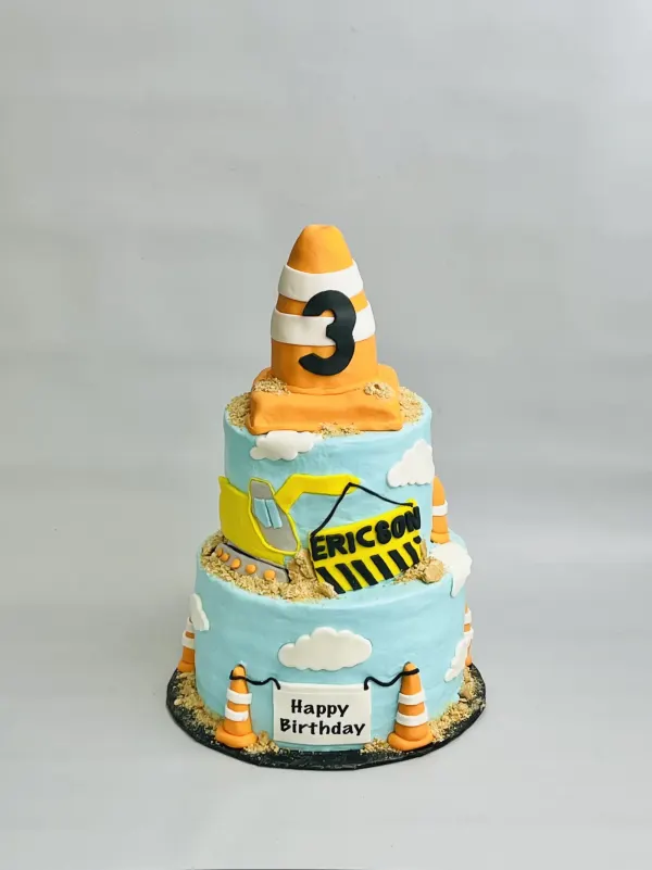 Two-tier construction cake with an excavator, traffic cones, a number 3 cone topper and Ericson sign