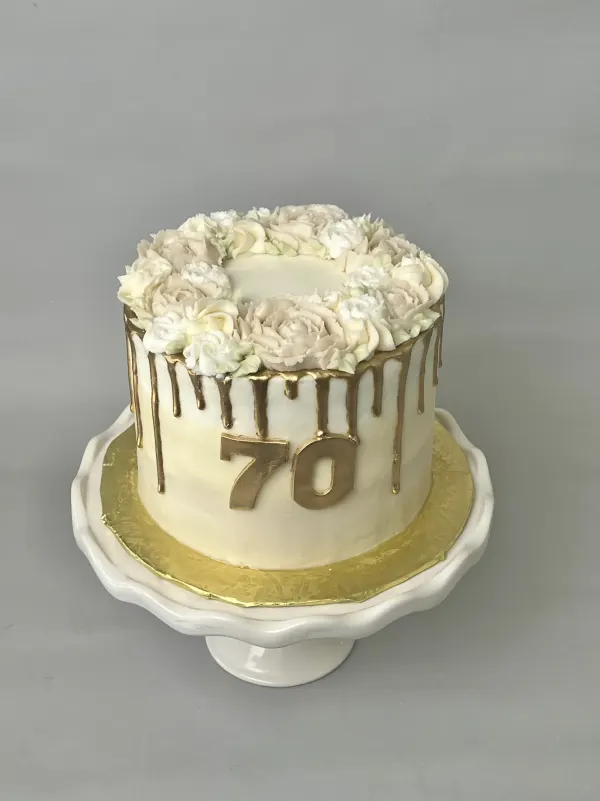 Ivory 70th birthday cake with a gold drip, buttercream flower crown and gold fondant 70