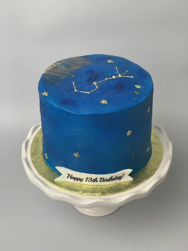 Deep blue constellation cake with gold stars and a banner reading Happy 13th Birthday