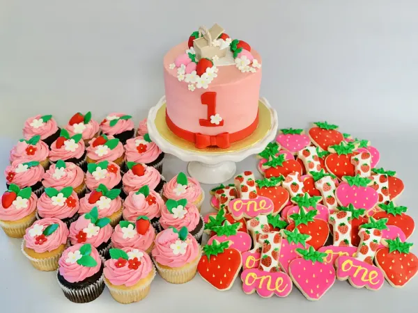 Strawberry first birthday set: pink cake with a red 1, berry cupcakes and one sugar cookies
