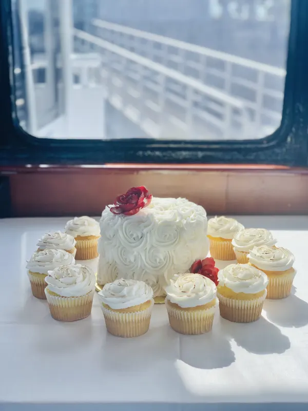 White buttercream rosette cake with red flowers, ringed by matching swirled vanilla cupcakes