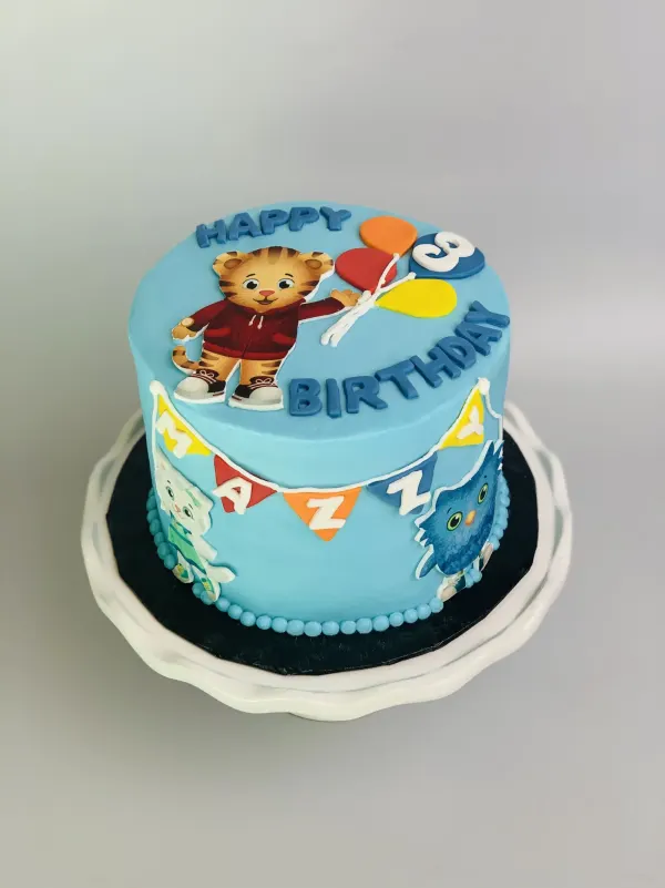 Blue Daniel Tiger third birthday cake with balloon cutouts and a Mazzy fondant bunting banner