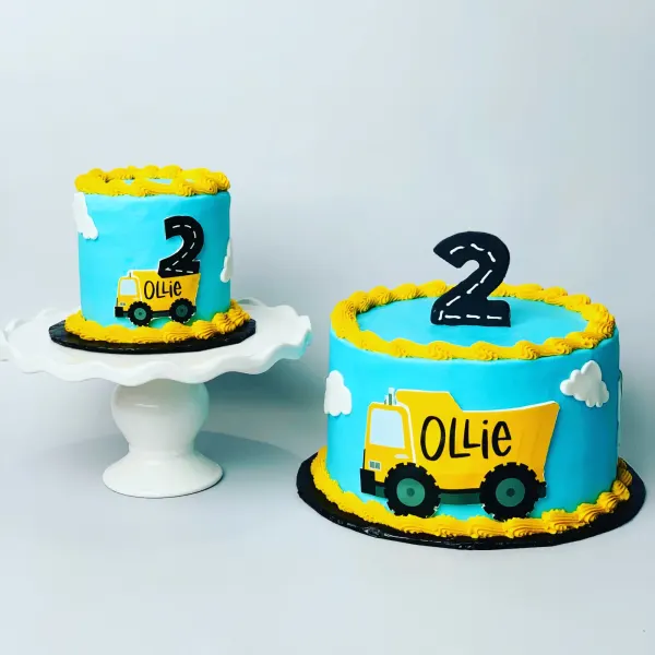 Pair of blue dump truck cakes with black road-stripe 2 toppers and Ollie on the truck bed