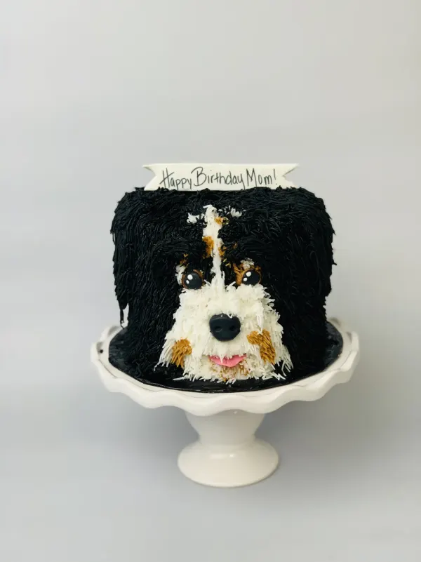Sculpted dog cake with piped black and white fur, a Bernedoodle face and Happy Birthday Mom