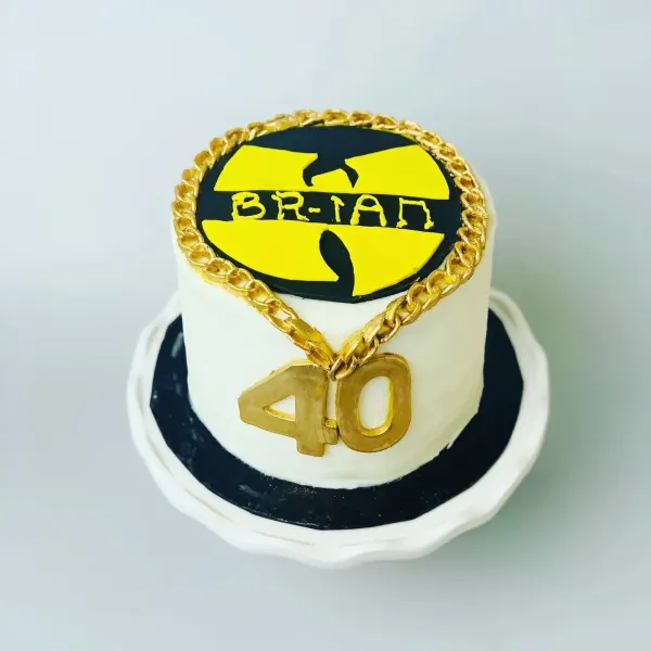 White cake with a yellow Wu-Tang logo reading Brian, an edible gold chain and a gold 40