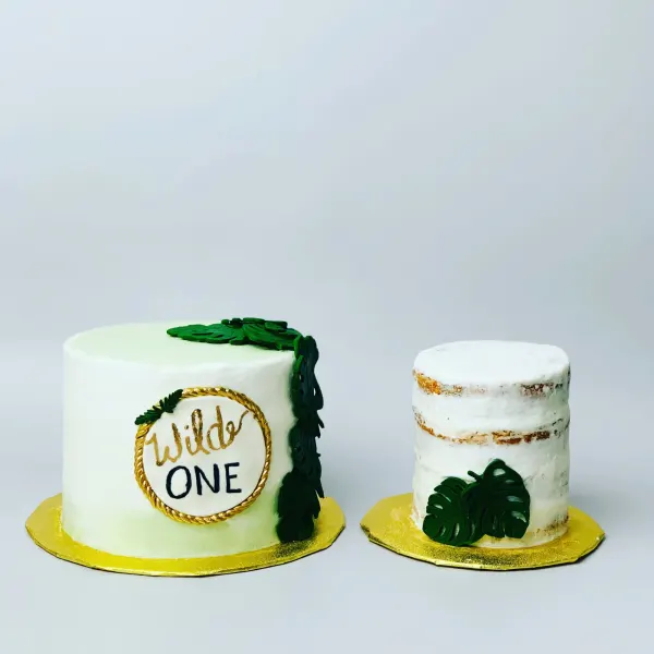 Pale green Wild One first birthday cake with monstera leaves and a semi-naked smash cake