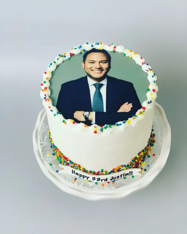 White birthday cake with an edible photo portrait, rainbow sprinkles and a Happy 33rd Justin banner