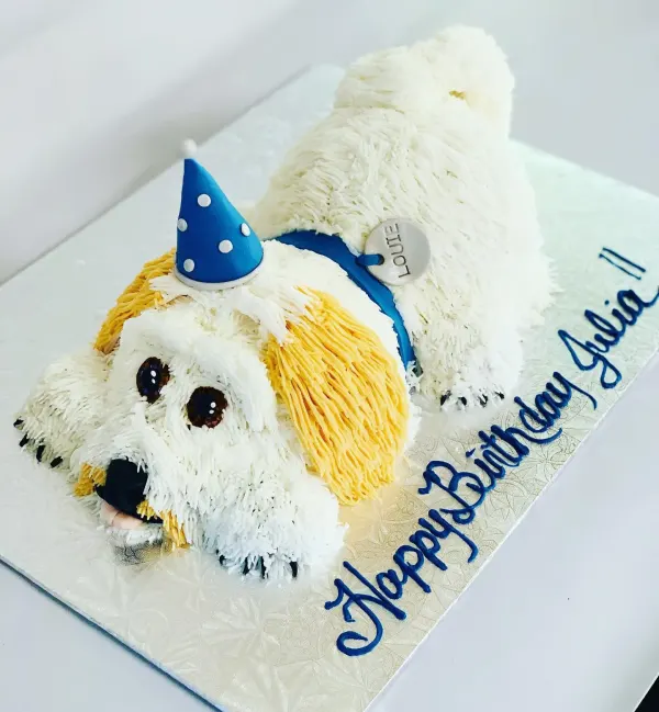 Sculpted dog birthday cake in piped white and gold fur with a blue party hat and Happy Birthday Julia