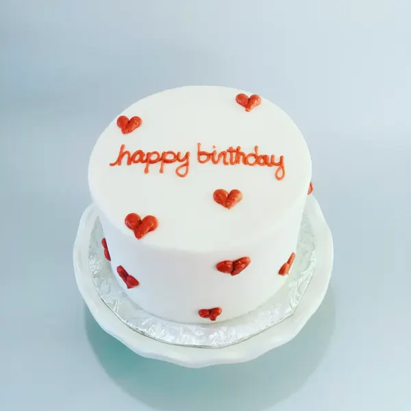 Round white fondant cake with piped red hearts and happy birthday in red script