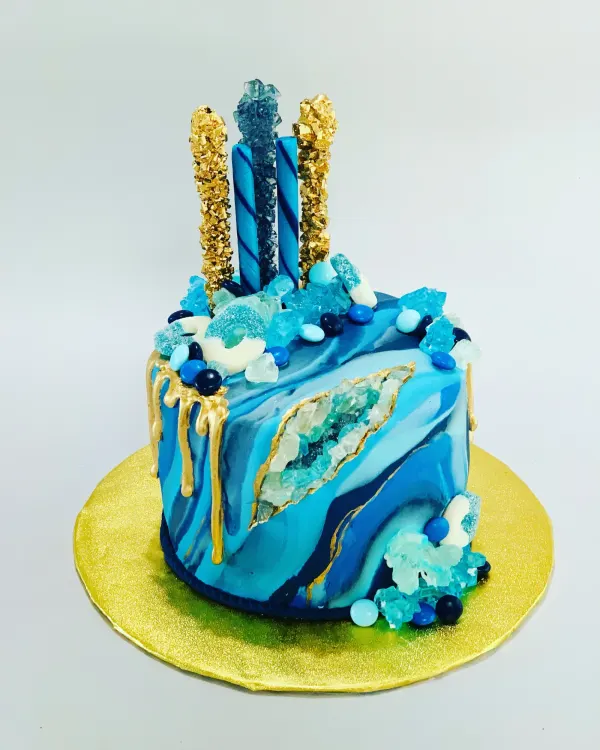 Blue marbled geode cake with rock candy crystals, gold drip and candy sticks on a gold board