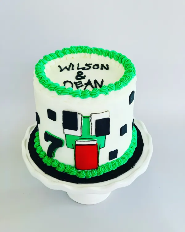 Minecraft creeper birthday cake in white buttercream with green piping, a number 7 and Wilson and Dean