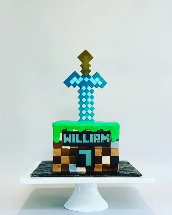 Minecraft grass block birthday cake with a diamond sword topper, the name William and a number 7