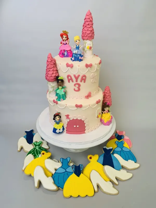 Two-tier princess castle cake with figurines, pink turrets, Aya 3 and decorated gown cookies