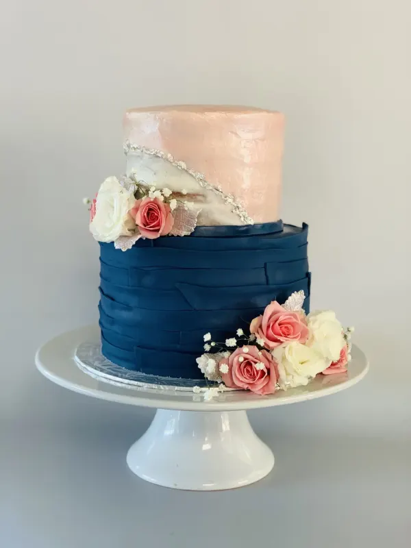 Two-tier cake with a blush top tier, navy pleated fondant base and fresh pink and white roses