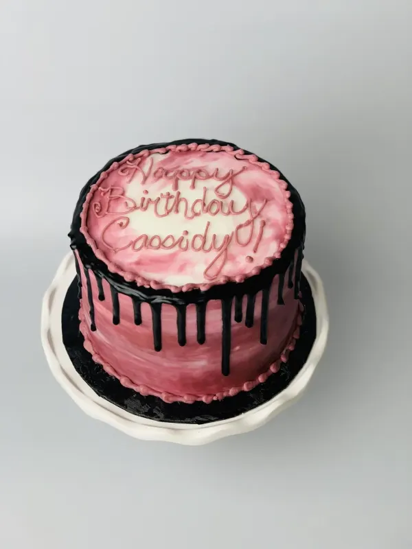 Pink marbled birthday cake with a black chocolate drip and piped Happy Birthday Cassidy