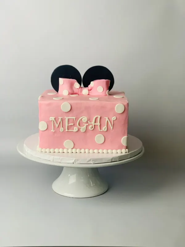 Pink Minnie Mouse birthday cake with fondant ears, a polka-dot bow and the name Megan