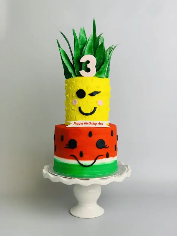 Two-tier pineapple and watermelon birthday cake with faces, a 3 topper and Happy Birthday Ava banner