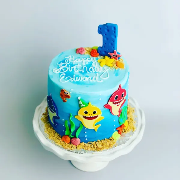 Baby Shark first birthday cake with shark cutouts, seashells and Happy Birthday Edward piped on top