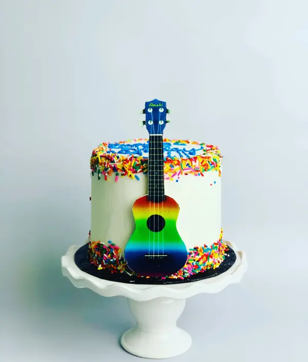 Birthday cake with rainbow sprinkles and a rainbow ukulele leaning against the side