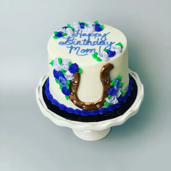 Birthday cake with blue and lavender buttercream roses, a copper horseshoe and Happy Birthday Mom