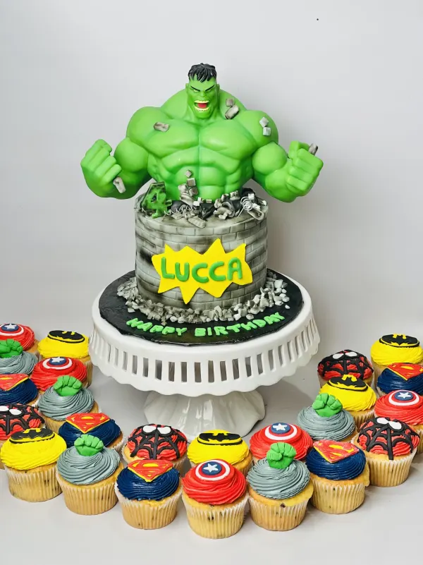 Incredible Hulk birthday cake with a brick wall finish, the name Lucca and superhero logo cupcakes