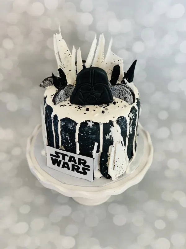 Star Wars drip cake with a black Darth Vader mask topper, white chocolate shards and Oreo pieces