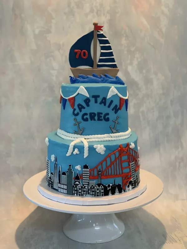 Two-tier nautical cake reading Captain Greg with a 70 sailboat topper and a San Francisco skyline