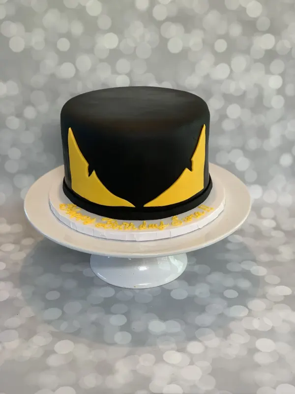 Black fondant cake with yellow bat-mask eyes and Happy Birthday Sina piped on the board